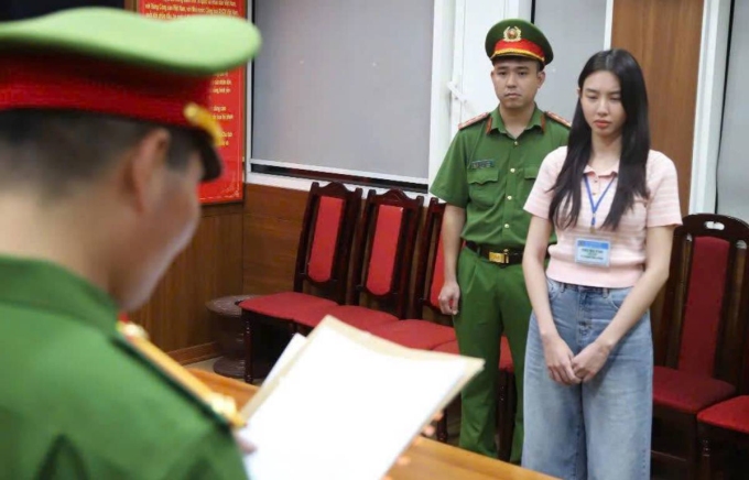 Hoa hậu Thùy Tiên (phải) nghe cảnh sát đọc lệnh khởi tố, bắt tạm giam. Ảnh: Bộ Công an