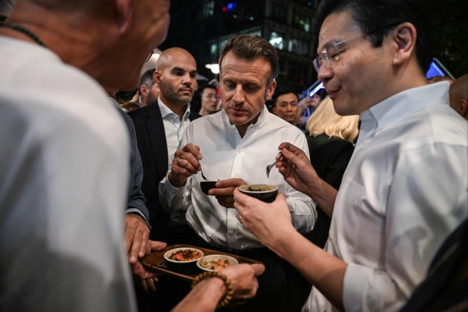 Tổng thống Pháp Macron (giữa) và Thủ tướng Singapore Lawrence Wong thưởng thức ẩm thực đường phố ngày 29/5. Ảnh: AFP