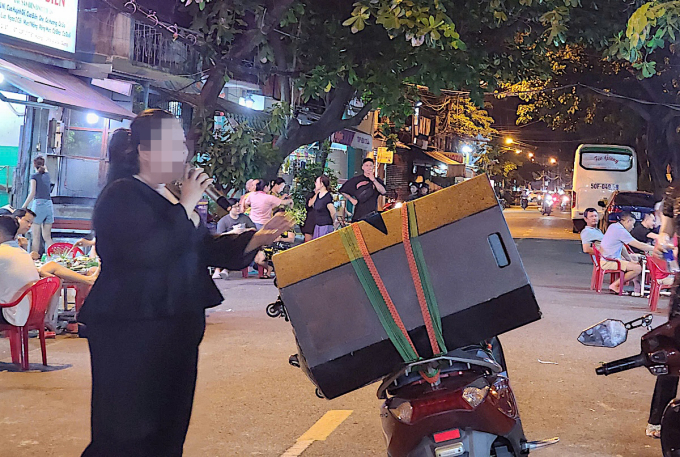 Người phụ nữ hát karaoke bằng loa di động đặt trên xe máy trước quán nhậu trên đường Thanh Đa, quận Bình Thạnh, tối 25/6. Ảnh: Đình Văn