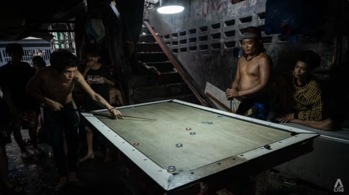 Một nhóm nam giới chơi bi-a chip trong một khu phố nghèo ở Metro Manila, nơi nhiều phụ nữ làm việc ở nước ngoài với tư cách là người giúp việc gia đình. Ảnh: CNA/Wisnu Agung Prasetyo