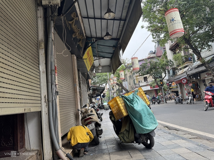 Một shipper phải cúi người sát mặt đất để lấy đơn hàng đem đi vận chuyển tại một cửa hàng thời trang trên phố Hàng Đào, quận Hoàn Kiếm, trưa 6/6. Ảnh: Quỳnh Nguyễn