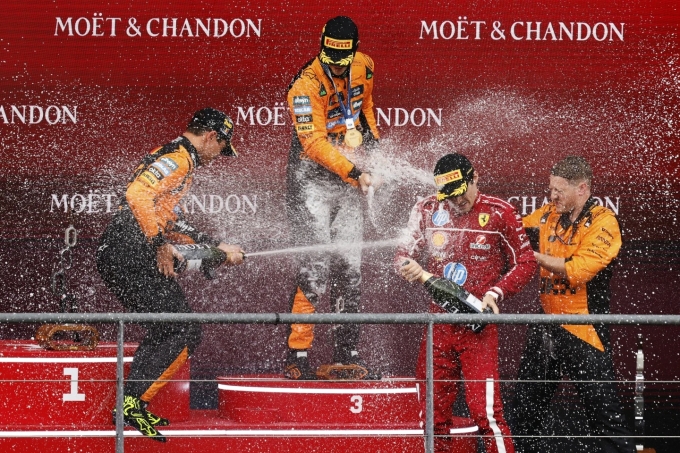Norris (trái) và Piastri (giữa) xịt champagne chúc mừng người về ba Leclerc (áo đỏ) trên podium Grand Prix Bỉ ngày 27/7. Ảnh: AP