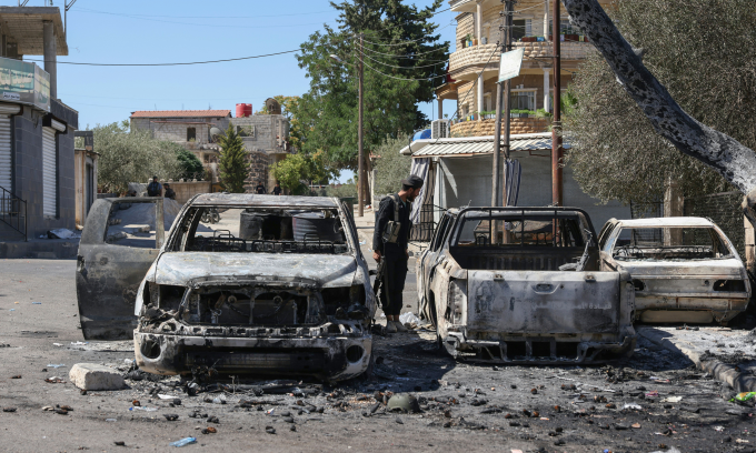 Thành viên lực lượng an ninh Syria bên cạnh xác ôtô bị cháy rụi tại Sweida hôm 16/7. Ảnh: AFP