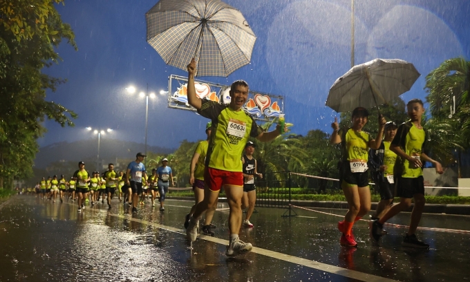 VĐV che ô dưới cơn mưa nặng hạt trên đường chạy VnExpress Marathon Hạ Long 2023. Ảnh: VnExpress Marathon