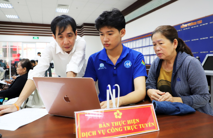 Lê Khánh (giữa) và cán bộ Trung tâm hành chính công phường Phú Nhuận, hỗ trợ bà Trang nhập thông tin lên Cổng dịch vụ công quốc gia, ngày 23/7. Ảnh: Lê Tuyết