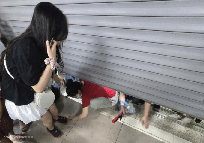 Một số hành khách cố tình chui qua khe cửa cuốn để vào nhà ga Cát Linh đêm 24/8. Ảnh: Gia Minh
