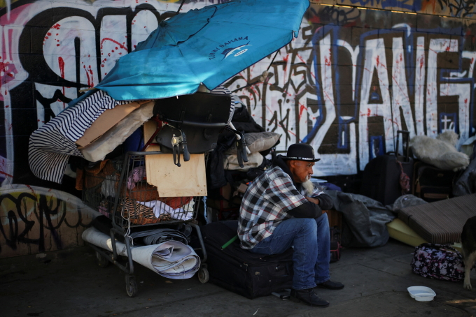 Một người đàn ông vô gia cư ngồi bên đường ở Los Angeles, bang California hồi tháng 12/2024. Ảnh: Reuters