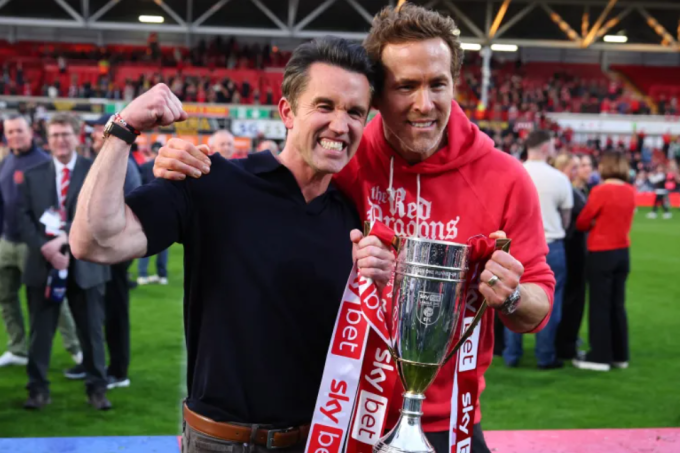 Các diễn viên và chủ sở hữu Wrexham Rob McElhenney (trái) và Ryan Reynolds ăn mừng với chiếc Cup vô địch, sau khi Wrexham thăng hạng lên Championship ngày 26/4/2025. Ảnh: Reuters