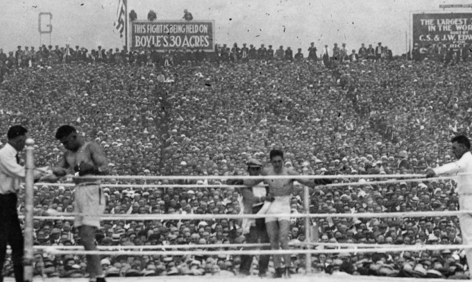 SVĐ chật kín khán giả, khi Jack Dempsey (trái) và Georges Carpentier nghỉ ngơi giữa các hiệp đấu trong trận đấu hạng nặng thế giới năm 1921. Ảnh: Tạp chí The Ring