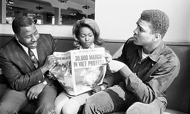 Muhammad Ali (phải) cầm tờ báo về một cuộc biểu tình của Mỹ để chống chiến tranh ở Việt Nam năm 1966. Ảnh: Bettmann Archive