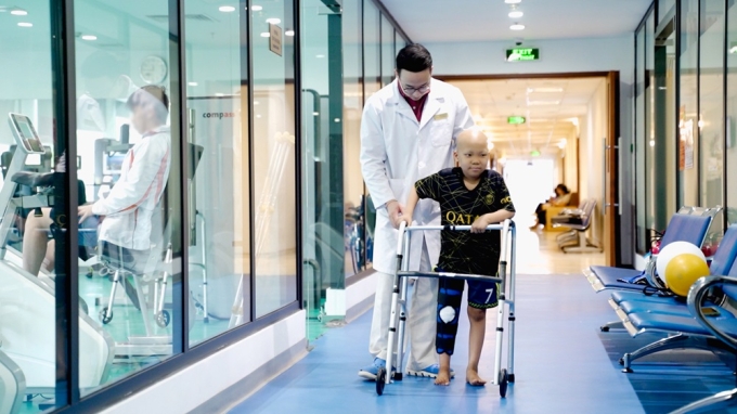 Hình ảnh bé Minh tập đi bằng dụng cụ hỗ trợ sau phẫu thuật